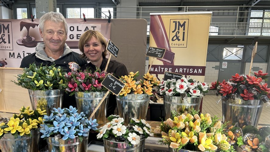 Deux exposants souriants derrière leur stand de maître artisan, garni de bouquets colorés