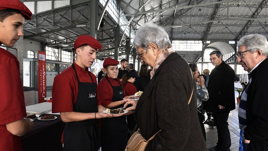 Élèves en tablier et béret rouge servant une dégustation de chocolat à une visiteuse